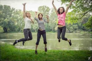 3 girls jumping by a pond smiling