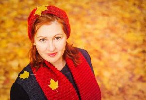 smiling woman with red hair red scarf and hat leaves falling
