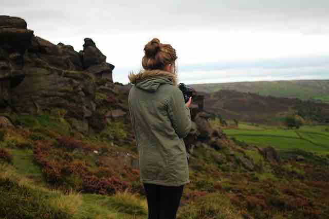 woman with a green coat on taking photos with a camera in the highlands